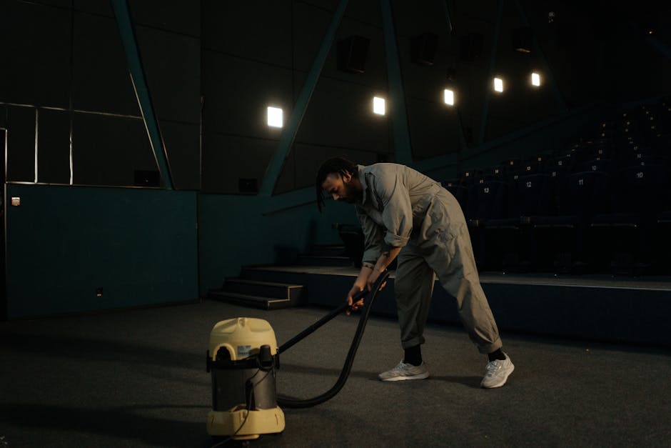 A person operating a yellow portable industrial blower on a patterned stone or tile floor, likely during a cleaning or drying process. The blower has a black grille for airflow, and the individual is holding it with both hands, focusing on surface cleaning or moisture removal. The surrounding environment appears to be an indoor space with a textured, multicolored stone or tile floor, and soft lighting highlights the clean surface. This scene exemplifies professional deep cleaning and surface sanitisation, typical of services provided by Cleaners St. John's Wood, aimed at ensuring hygienic and spotless interiors.